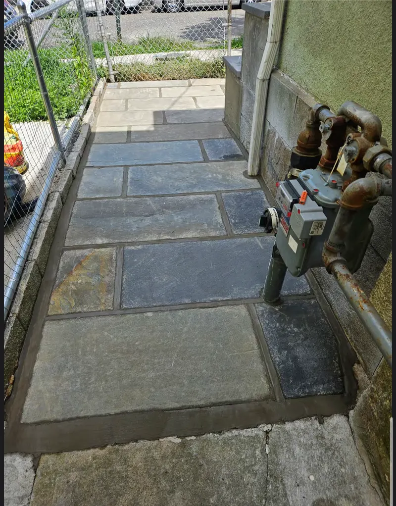 A narrow side-yard passage newly paved in mixed grey and blue bluestone, running between a fence and a building wall.