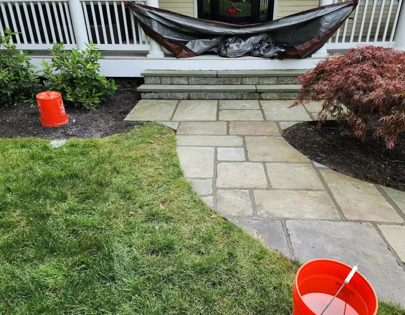 A curved bluestone walk in mixed rectangular pieces leading to granite block steps at a covered porch.
