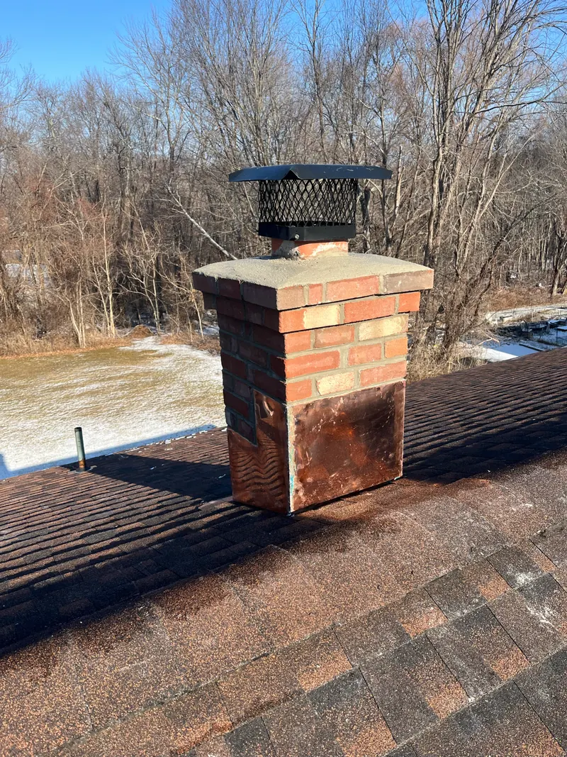 A rebuilt brick chimney on a shingle roof with a new mortar crown, copper flashing and a black cap.
