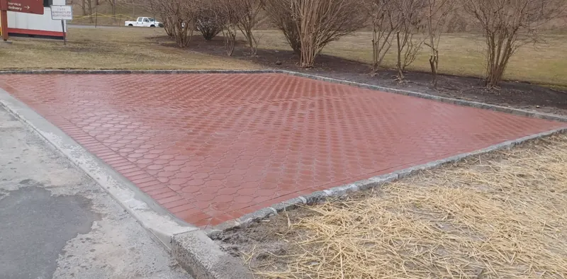 A large red interlocking paver apron with a granite curb edge at a commercial service entrance.