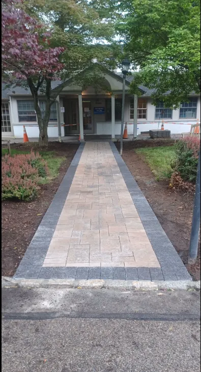 A straight paver entry walk with a darker charcoal border leading to the covered entrance of a low public building.