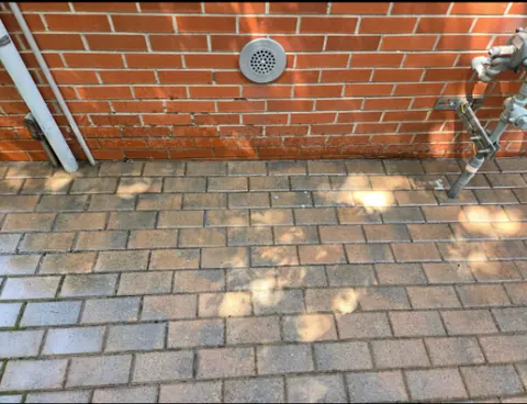 A brick-coloured paver terrace running along the base of a red brick wall.